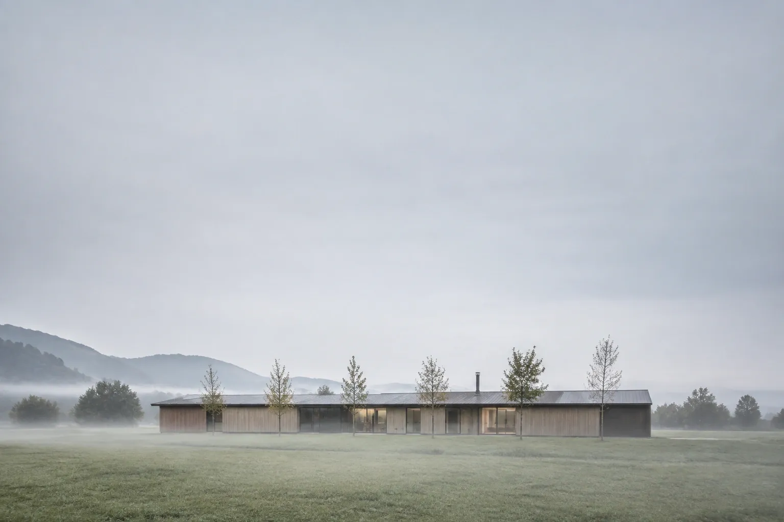 Casa in legno bassa e allungata in un prato, con la nebbia del mattino