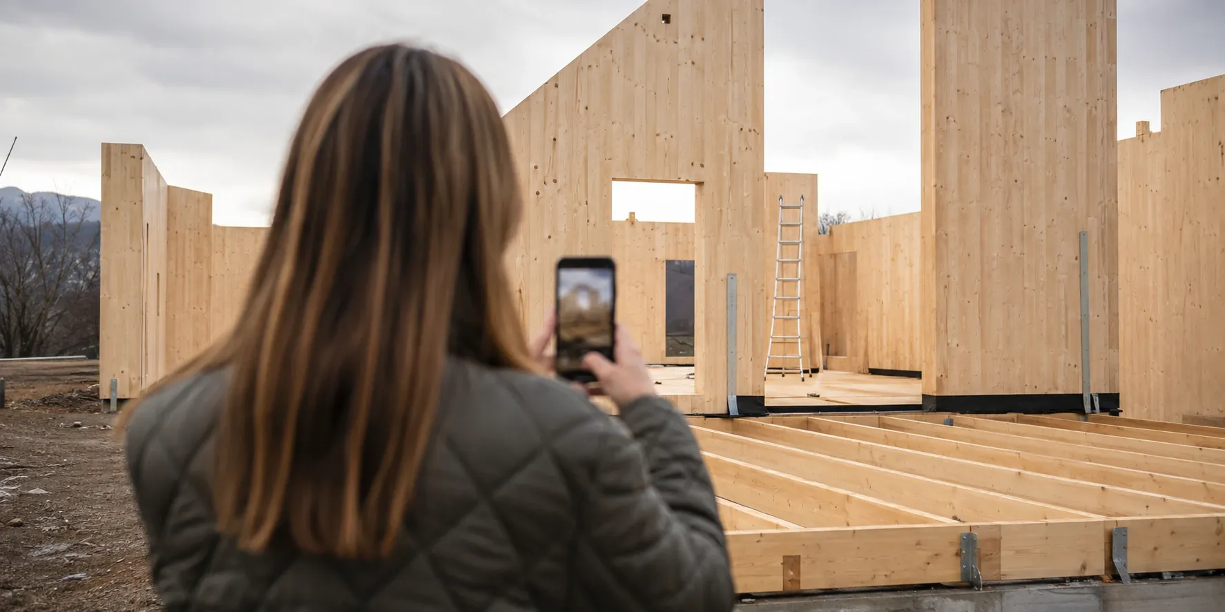 Una donna in cantiere consulta il telefono davanti alla struttura in legno