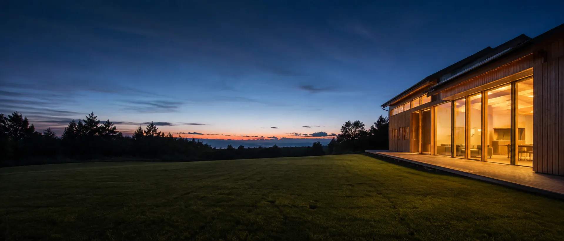Casa in legno al tramonto, la luce interna si posa sulla terrazza